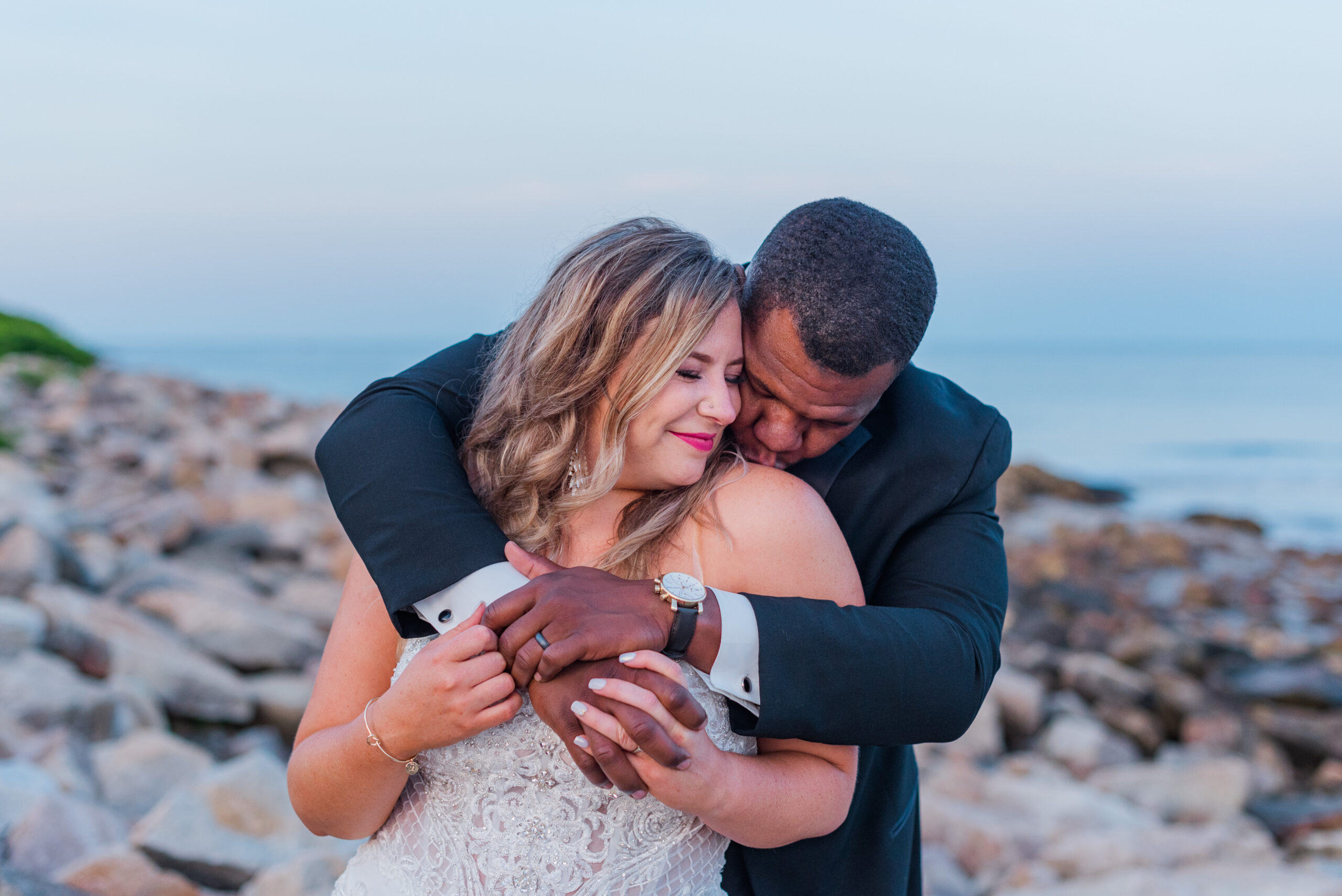 Bride and groom embracing along Maine coastline at sunset wedding